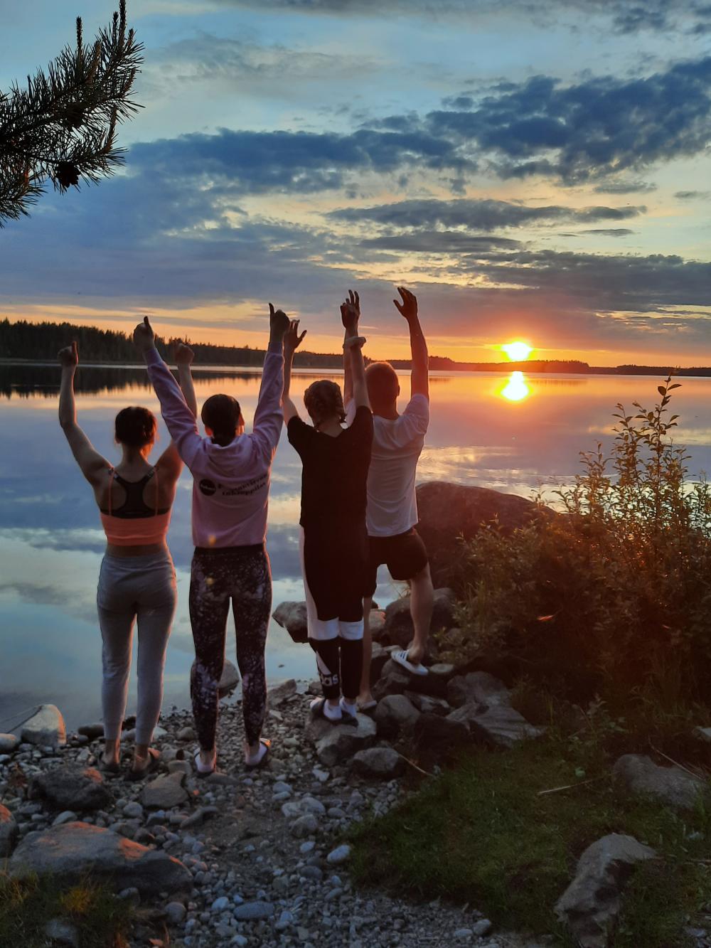 Neljä nuorta seisoo järven rannalla. Kaunis auringonlasku.